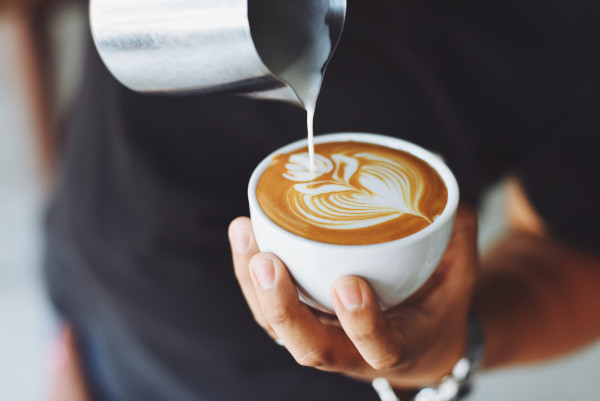 Foto de barista haciendo una forma de hoja en la taza de café con la leche y la espuma